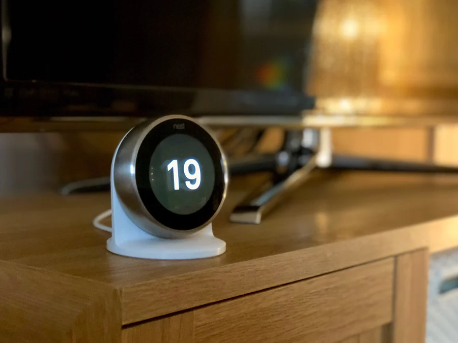 A third generation Nest Learning Thermostat standing on a stand on a cabinet.