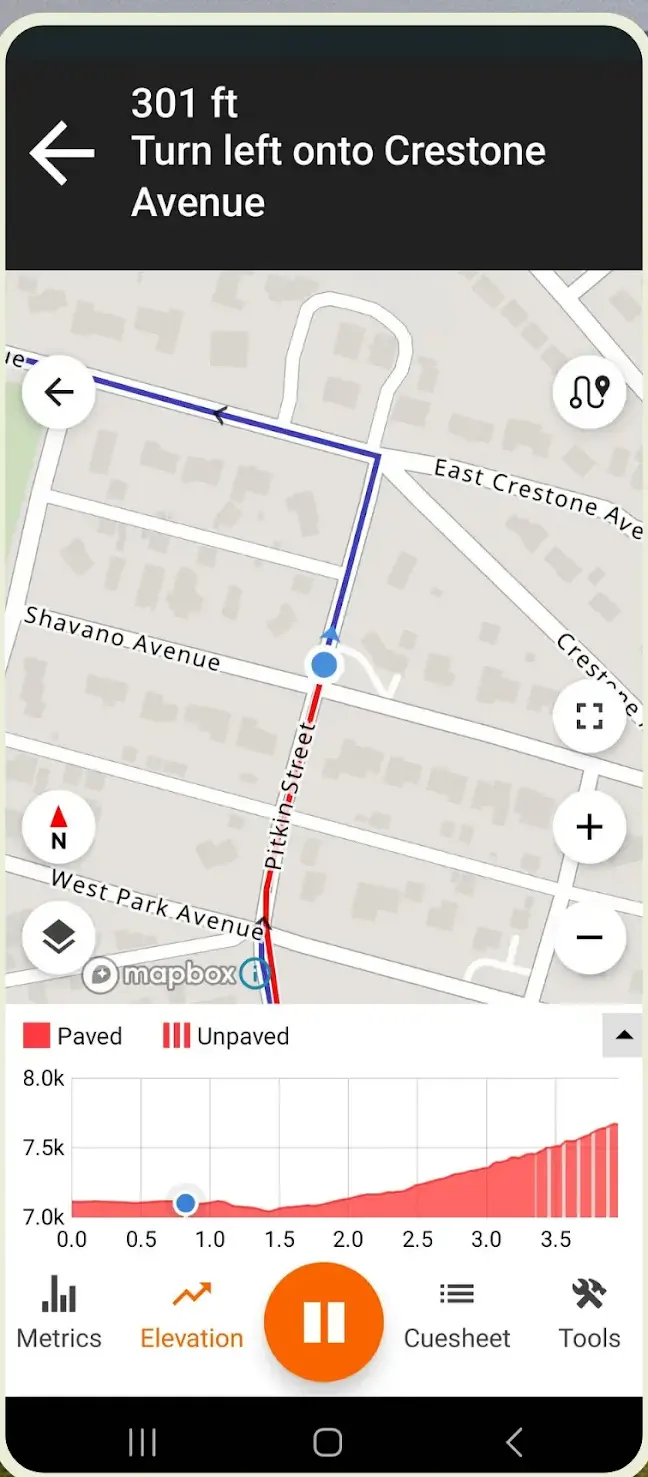 A Ride with GPS navigation screen showing the instruction "301 ft, turn left onto Crestone Avenue" above a street map with the planned route in blue, a paved/unpaved elevation profile along the bottom, and tabs for Metrics, Elevation, Cuesheet and Tools.